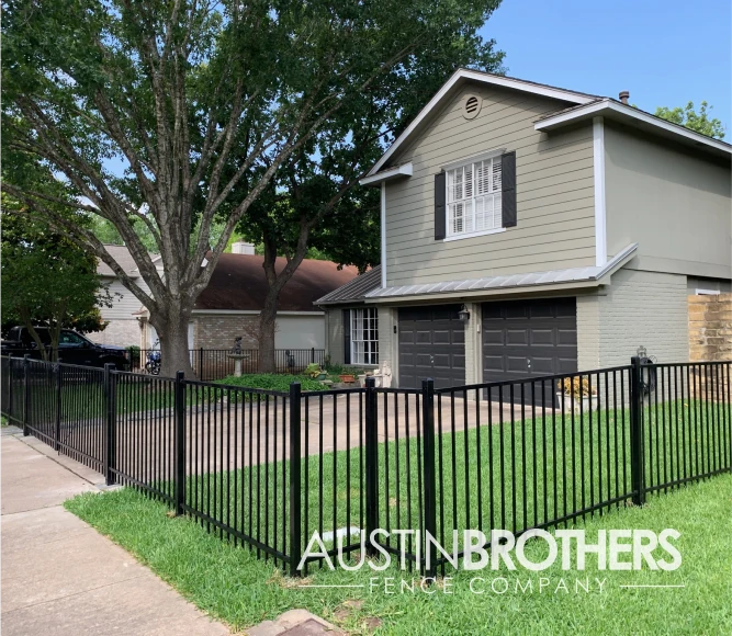 Waist-high black iron fence blocking off a front yard and driveway.