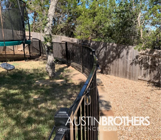 Black iron fence rounding a curved retaining wall.