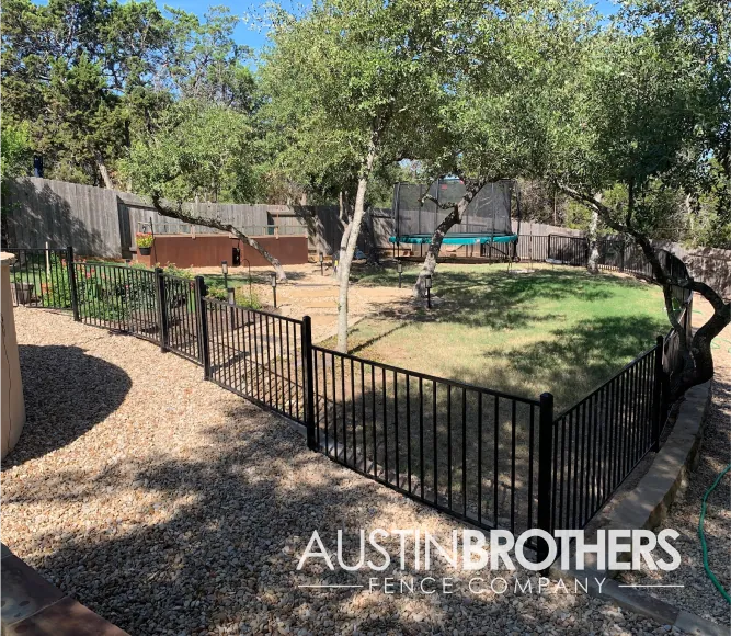 Black iron fence rounding a retaining wall and separating a back yard area.