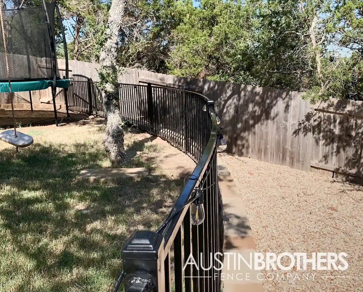 Iron fence curving around a retaining wall in an Austin, Texas backyard.