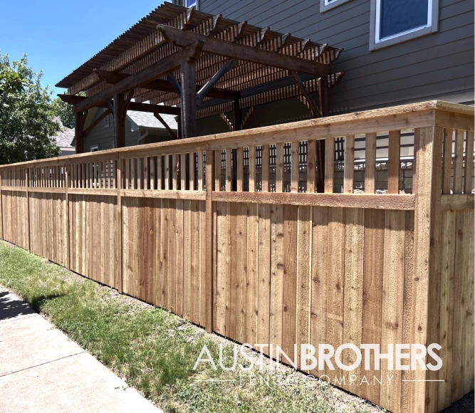 Capped vertical wooden fence with a pergola behind it.