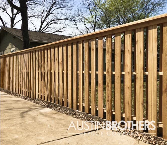 Capped vertical wooden fence with breaks between the slats.