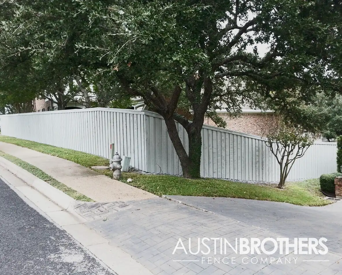 White vertical fence blocking off a backyard from a neighborhood street.