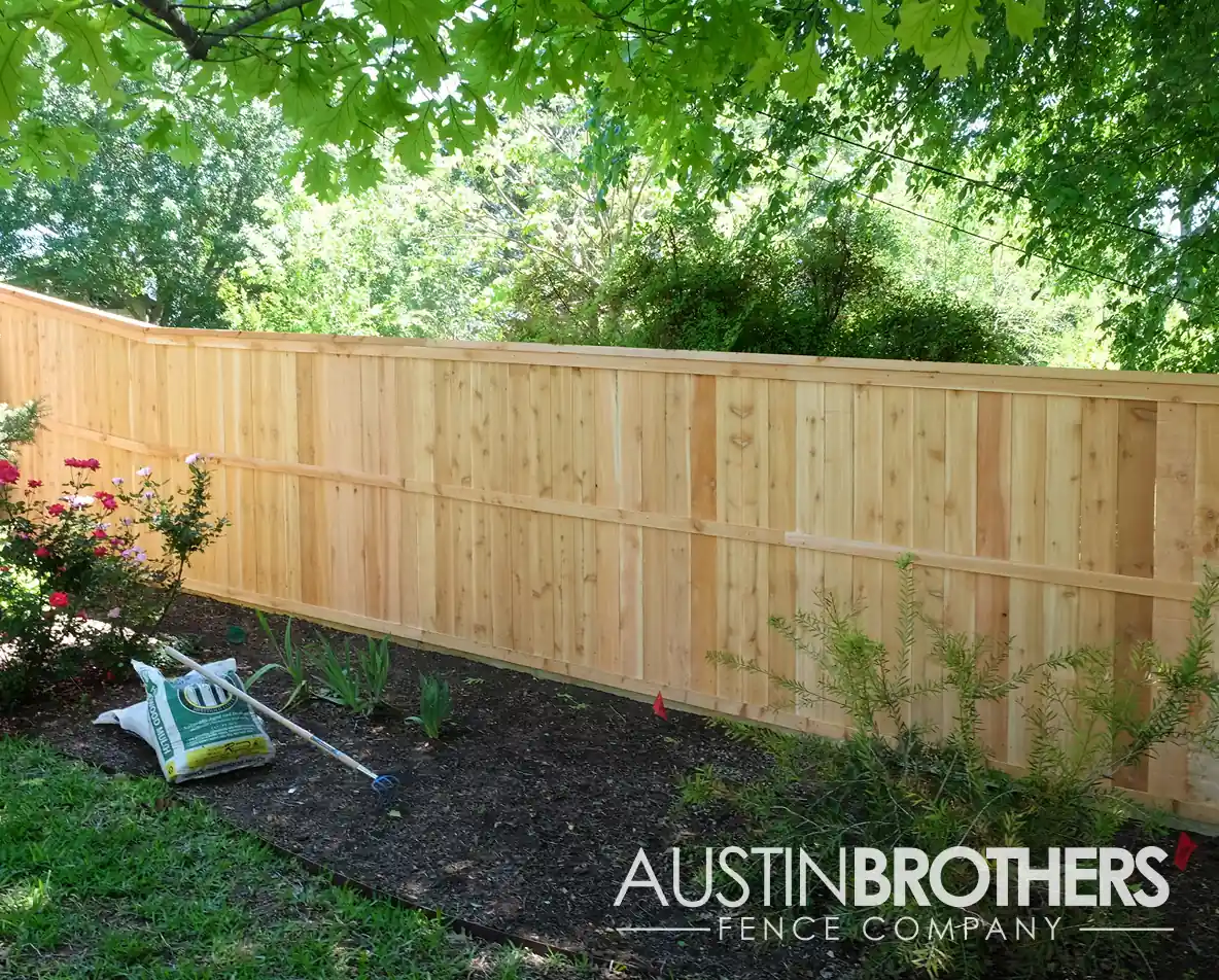 Vertical wooden fence with reinforced rails running alongside a flower bed.