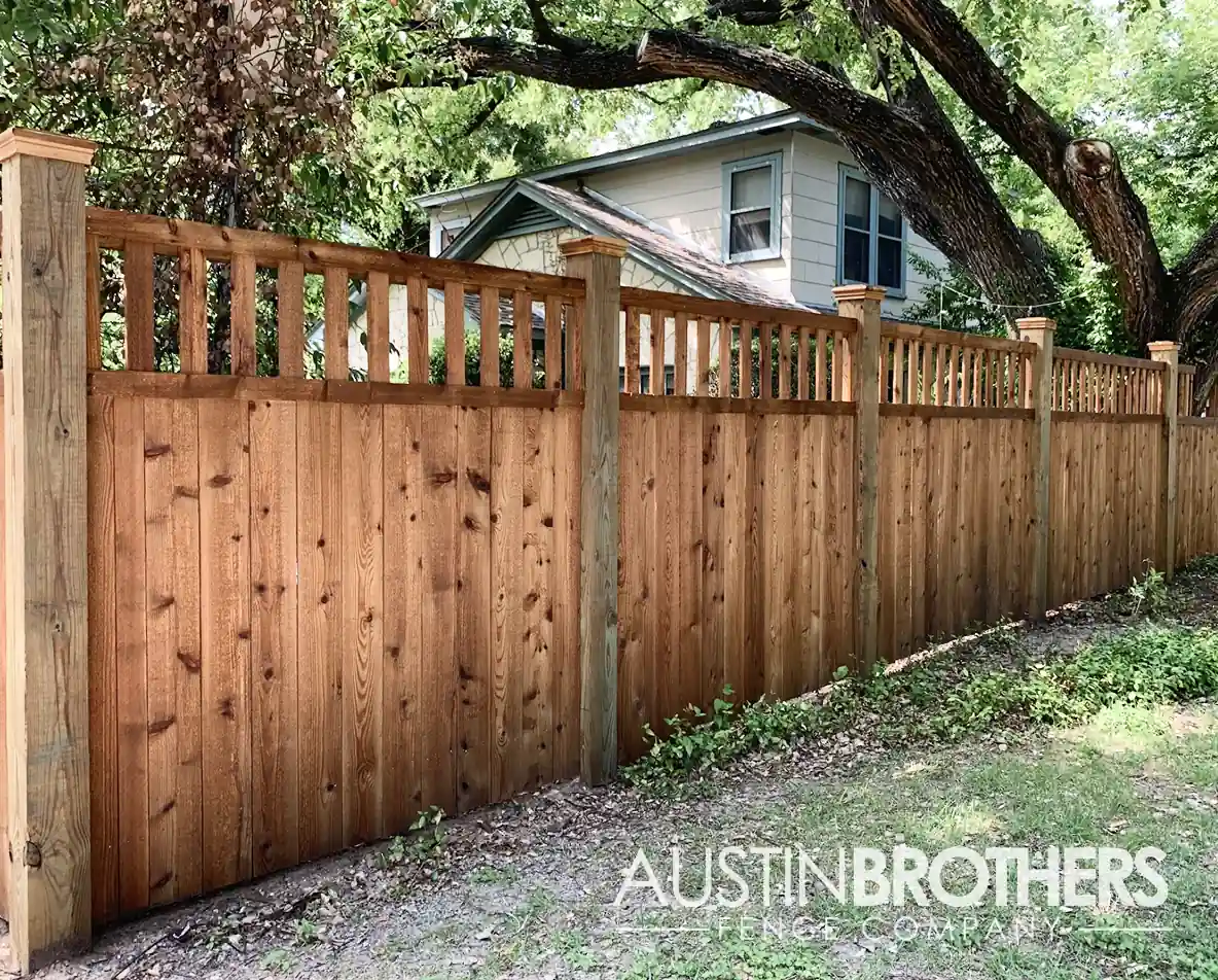 Vertical cedar fence with a decorative top in front of a two-story house.