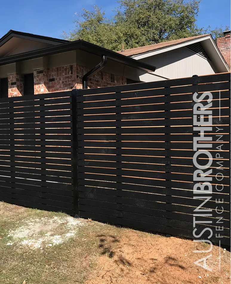 Horizontal wooden fence, stained black, in the back yard of an Austin, Texas home.