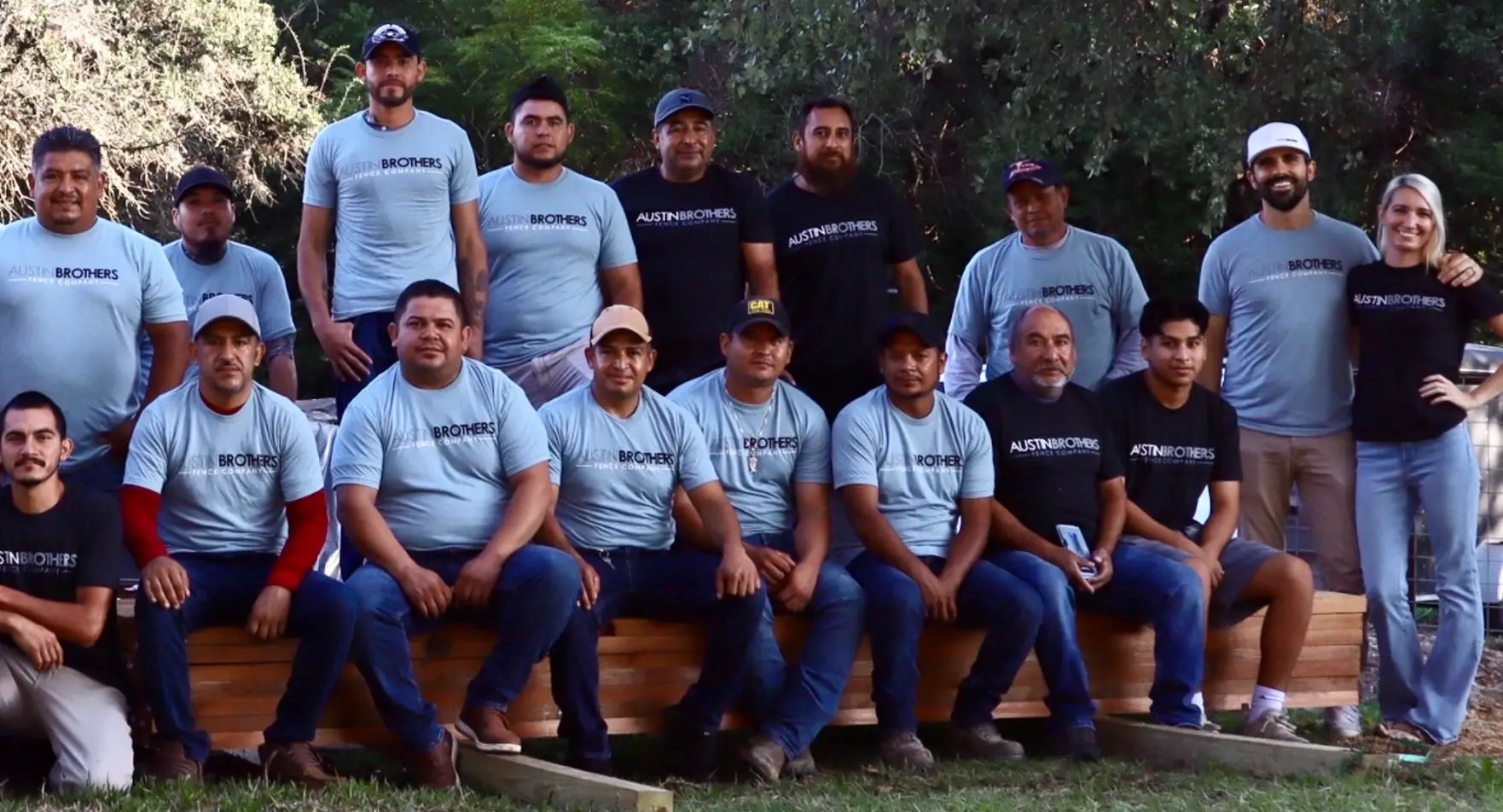 The whole Austin Brothers Fence Company team in matching shirts, sitting and standing around a fence.