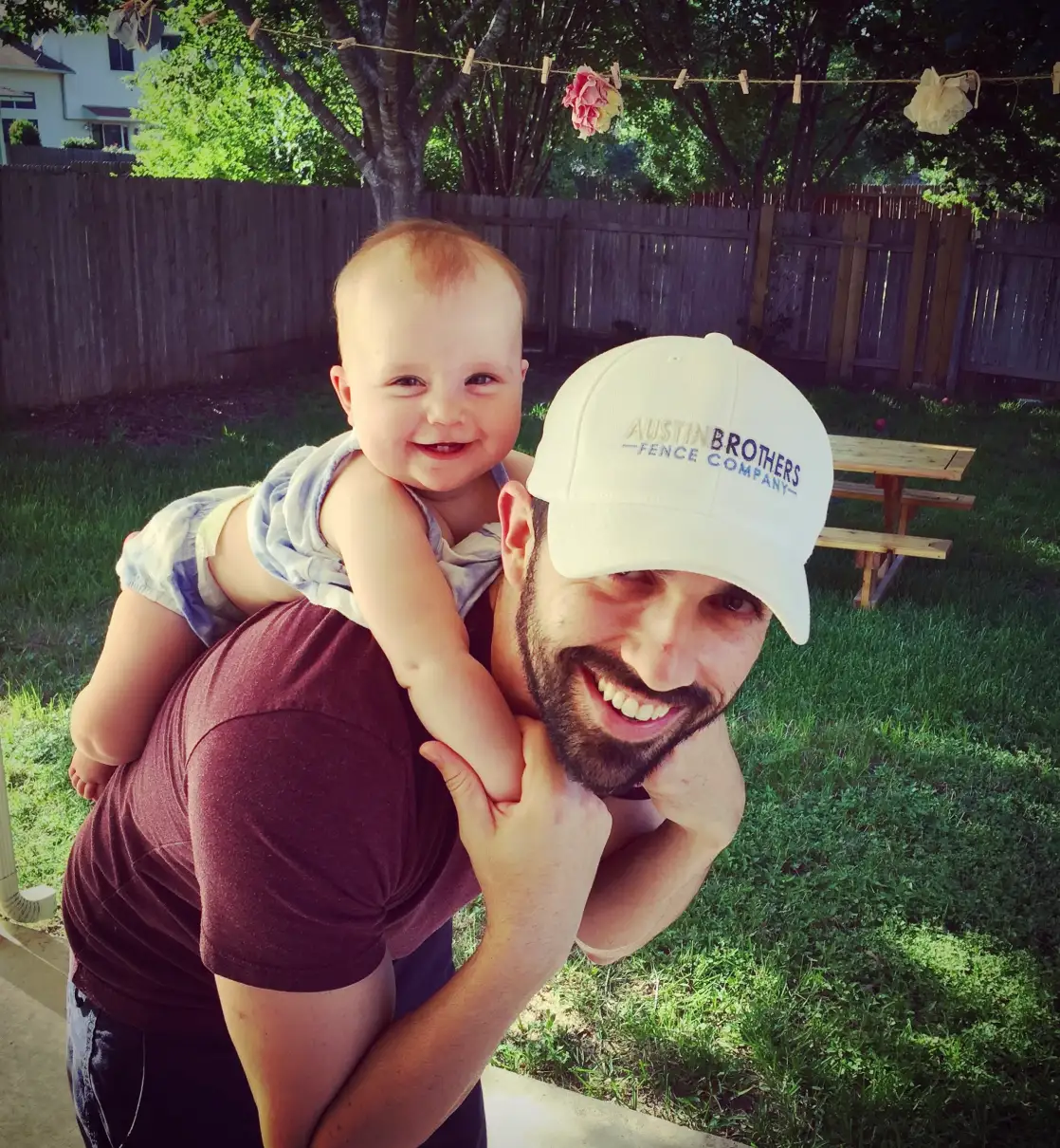 Nate Austin smiling in an Austin Brothers cap, carrying a baby on his shoulders.